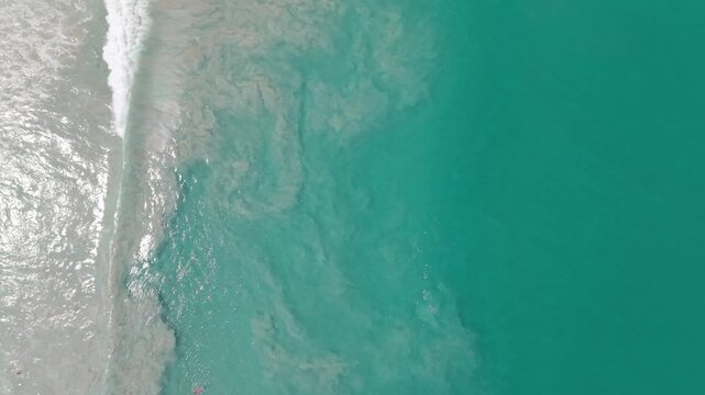 Aerial view of ocean waves crashing onto a sandy beach, with visible ripples and foam patterns forming in the turquoise water, showcasing the dynamic interaction between land and sea