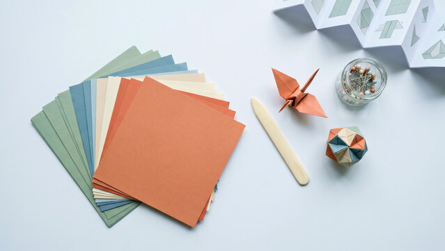 Origami paper craft supplies colored sheets crane models on white overhead flat lay, origami paper craft concept, paper folding supplies overhead, origami kit flat lay, paper art supplies