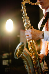 Obraz premium A musician performs a golden saxophone solo during a live evening concert. Their hands expertly press the keys, fingers moving gracefully over the instrument.