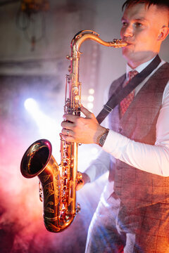 A professional musician performs a golden saxophone solo amidst stage lights and smoke at an industrial jazz concert