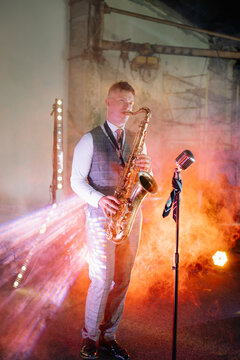 A male musician plays a golden saxophone solo on a smoky, spotlighted industrial stage for a moody, soulful jazz performance