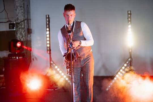 A professional male saxophonist in a formal grey suit performs a soulful jazz solo under bright stage lights at an evening private event