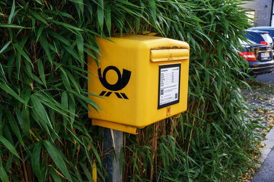 Iserlohn, Germany - July 12, 2026: Yellow Deutsche Post mailbox beside bamboo plants on a street