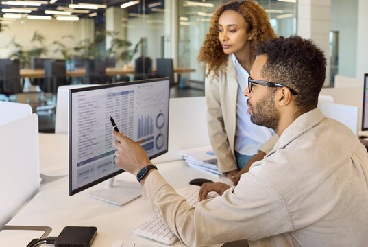 Analysts team meeting discussion in office. Two colleagues review data on a computer monitor with charts, aligning reporting and collaboration to forecast performance. Business analysis concept.