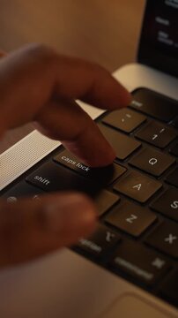 Finger Pressing Caps Lock Button on Laptop Keyboard in Warm Lighted Room.
