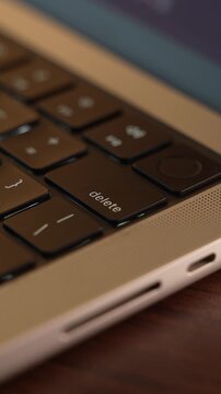 Finger Pressing the Delete Button on a Laptop Keyboard in a Warm Lighted Room.
