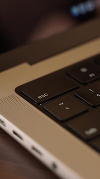 Finger Pressing Escape Key on Laptop Keyboard in Warm Lighted Room
