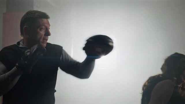 Young Caucasian female boxer punching focus mitts during training with middle aged Caucasian male coach. Ideal for fitness marketing and sports training campaigns
