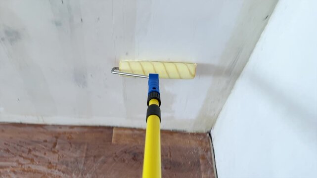 Applying liquid primer coat to wall with roller on extension pole