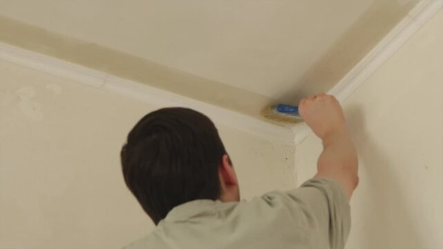 Back view of young man applying anti mold primer to ceiling corner