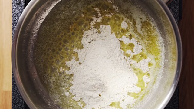 Flour pours into melted butter, starting homemade gravy. Gravy will thicken into rich, savory sauce once fully cooked. Gravy goes well with turkey, lamb, meatballs, chicken and mashed potatoes.