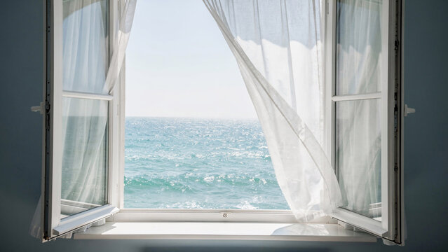 Open window revealing tranquil ocean view with gentle white curtains blowing in the breeze, perfect for travel, summer and relaxation advertising