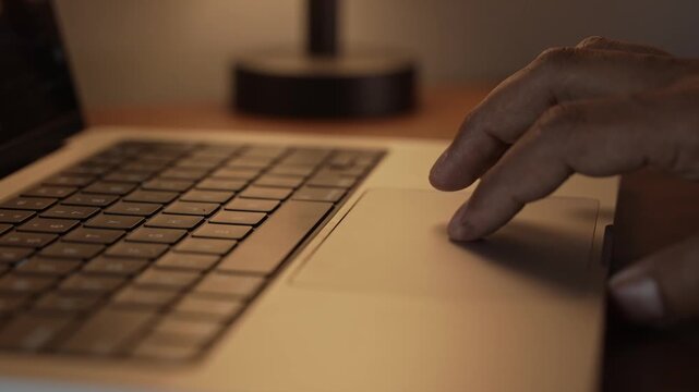Hand Using Laptop Trackpad in Warm Cozy Lighted Room.
