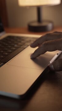 Hand Using Laptop Trackpad in Warm Cozy Lighted Room.
