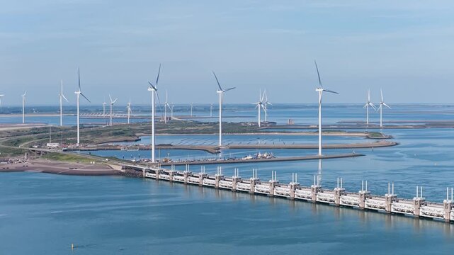 Aerial drone view of a Dutch storm surge barrier with wind turbines. The Netherlands. Wind mills generate green electricity near a massive dam and water stream.