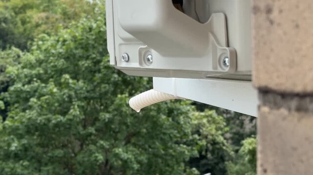 Close up of water dripping from an air conditioner drain pipe summer against a backdrop of green trees. Maintenance and repair concept