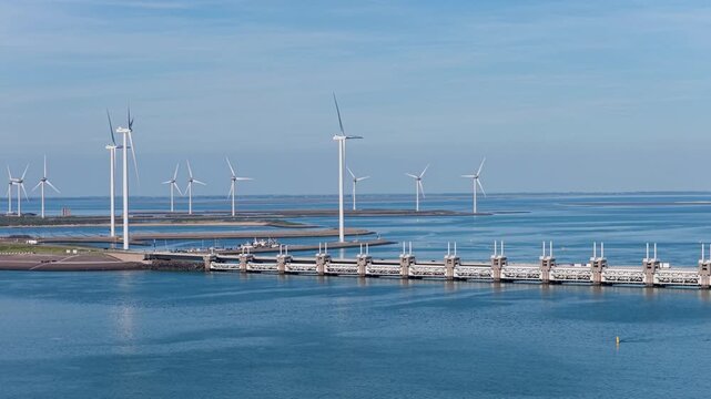 Aerial drone view of a Dutch storm surge barrier with wind turbines. The Netherlands. Wind mills generate green electricity near a massive dam and water stream.