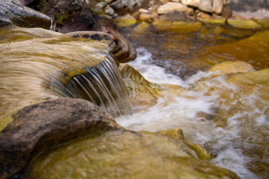 Clear river flowing over layered rock formations and quartzite stone beds in Ibitipoca, Minas Gerais, Brazil