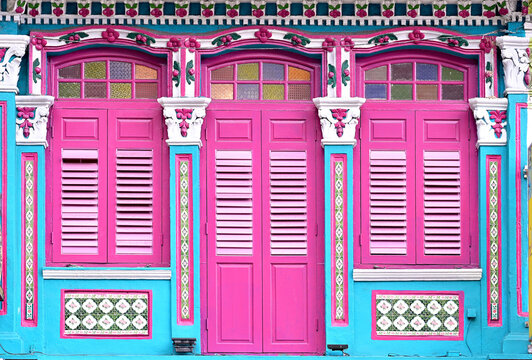 Blue Singapore Straits Chinese Peranakan shop house exterior with arched windows, pink louvered shutters and ornate columns with floral trimmings