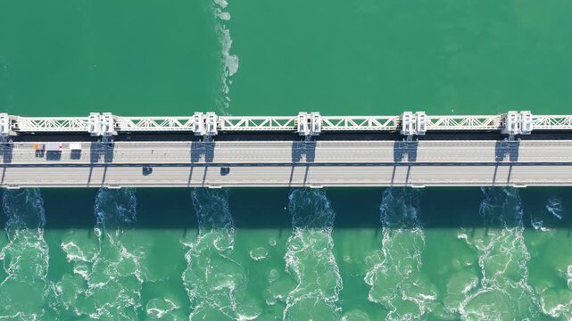 Aerial drone view of a massive storm surge barrier in the Netherlands. Powerful water stream flowing through the opened dam gates in an industrial coastal landscape.