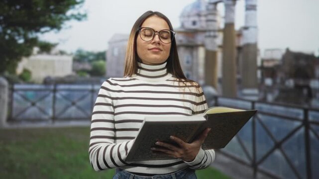Woman holds open book with hands and closes eyes in front of ancient building; serenity introspection.