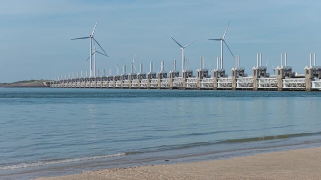 Aerial drone view of a Dutch storm surge barrier with wind turbines. The Netherlands. Wind mills generate green electricity near a massive dam and water stream.