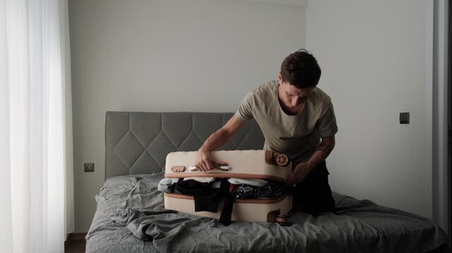 Packing stress and overloaded luggage. Man forcing overflowing clothes into suitcase before travel or relocation, illustrating poor packing and authentic home routine