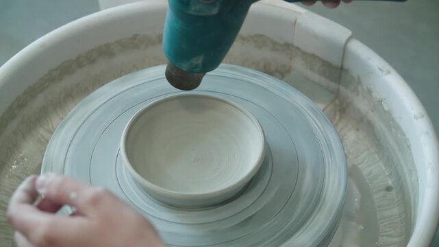 Close-up of clay billet on potters wheel is dried with construction hair dryer. Handmade work. master class. Crafting, artwork and handmade concept