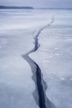 Deep Crack on Frozen Ice Surface of Winter Lake Stretching to Horizon