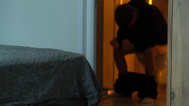 Man experiencing irritable bowel syndrome symptoms while sitting on toilet at home, chronic digestive disorder and gut health concept