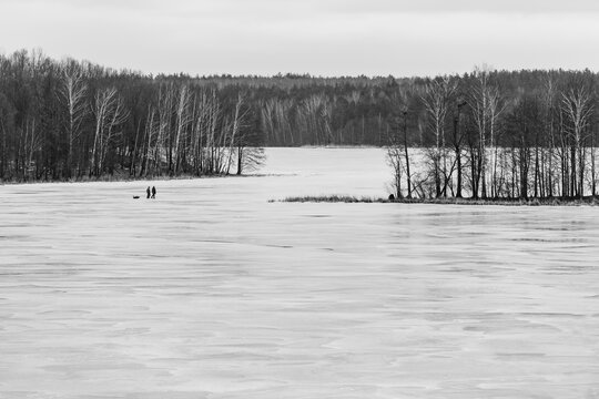 Dense Dark Forest Background Behind Two People on Frozen Winter Lake