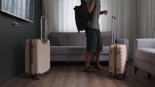 Constant moving and temporary housing lifestyle. Man arriving with luggage and sitting on sofa in empty apartment