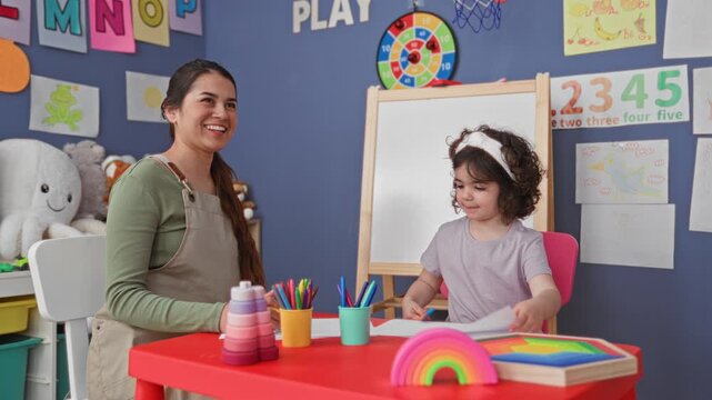 Woman teacher guides girl drawing with crayon at a small table in a classroom building surrounded by toys and an easel; learning nurturing calm.