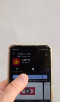 Tbilisi, Georgia - July 24, 2026: Vertical photo. Male hand holds mobile phone with Google app store open. Installing Russian payment system Golden Crown or KoronaPay, used for money transfers
