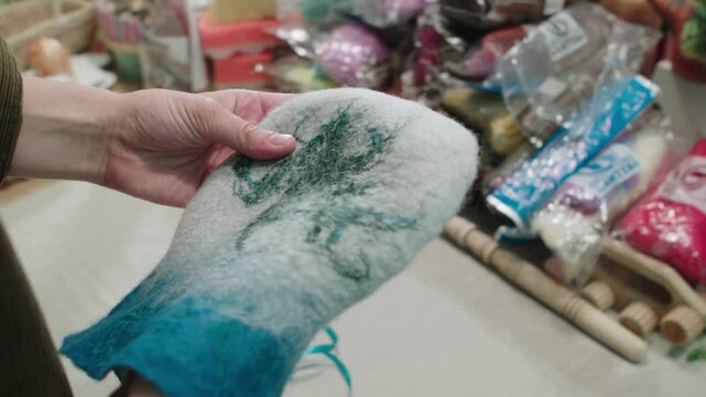 Envelope, bath hat, storage bag. Woman touches delicate, soft product made of felted wool against backdrop of souvenir workshop. Homecraft hobby