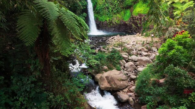 Aerial view of a waterfall cascading through basalt columns. Water plunges into a deep, narrow gorge. Rugged, jagged cliffs frame the falling stream. Exposed earth and stone surround the dramatic drop