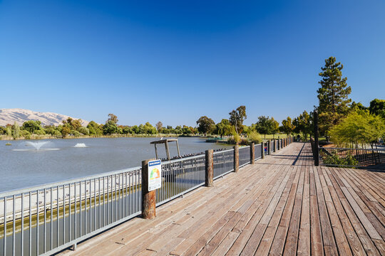 Wooden boardwalk and railing view across Lake Elizabeth in Fremont California Central Park on clear day