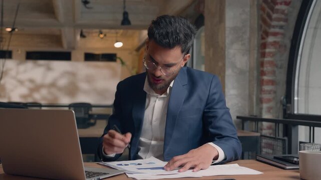 Arabian business man analyze laptop document data businessman writing notes in paper stats diagram in office male analyst Indian focused guy executive CEO write graph information looking in computer