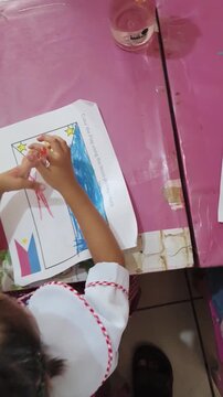 Child colors Philippine flag with red marker on paper at pink table