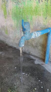 Water flows steadily from a blue outdoor faucet against a mossy wall.