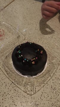Child reaches for chocolate cake with colorful sprinkles on clear plastic plate