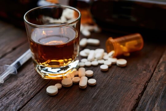 The Whiskey Glass with Pills on a Wooden Table at Night