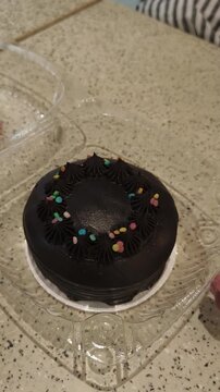 Hand reaches for chocolate cake topped with colorful sprinkles and piped frosting