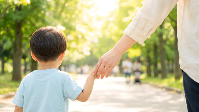 新緑の公園でしっかりと手をつないで散歩する親子の後ろ姿の手元