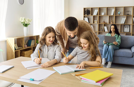 Father helps daughters with homework and studying. At home the family values learning and education, with a parent guiding children at the table. Concept: family learning and parental support