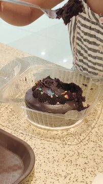 Child eats chocolate cake with colorful sprinkles using a spoon.