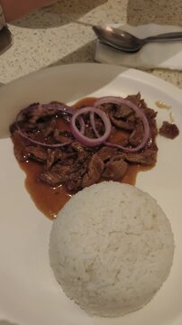 Person eats beef with onions and rice on a white plate.