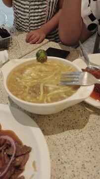 Person eats soup with fork from white bowl on speckled table