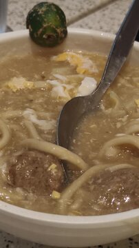 Spoon stirs noodles and meatballs in savory broth with lime garnish