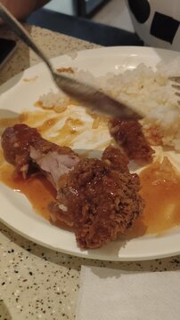 Person eats fried chicken and rice with spoon on white plate